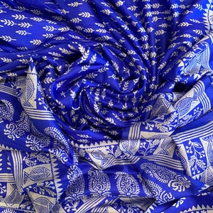 May include: Blue silk fabric with a white floral pattern. The fabric is folded and draped, showing the intricate details of the design.