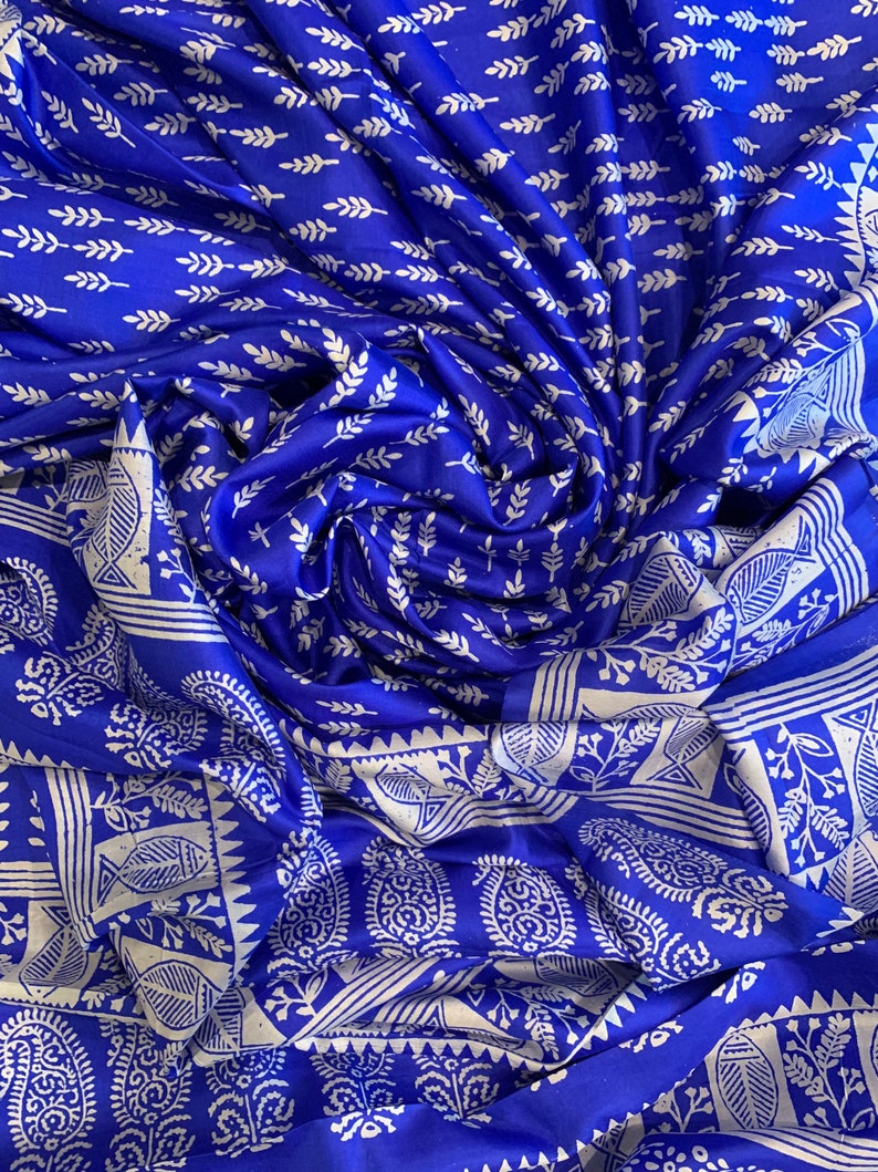 May include: Blue silk fabric with a white floral pattern. The fabric is folded and draped, showing the intricate details of the design.