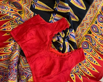 May include: A red sleeveless blouse with a decorative neckline and white pom-poms. The blouse is laid on top of a colorful fabric with a geometric pattern.