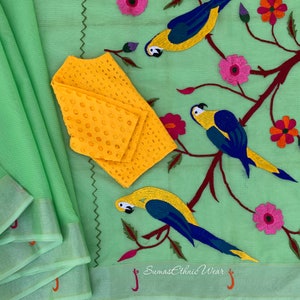 May include: A green cotton saree with a yellow embroidered blouse and a parrot design. The saree has a light green border and the blouse has a floral design. The saree is decorated with parrots and flowers.