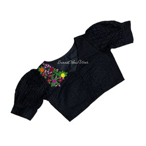 May include: Black blouse with embroidered floral detailing. The blouse features a V-neck and short, puffed sleeves. The floral embroidery includes orange, purple, red, pink, and yellow flowers with green leaves. The text "Sumas Ethnic Wear" is visible on the blouse.