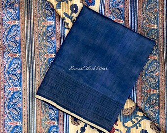 Pode incluir: Um sari de seda azul marinho com uma borda estampada em creme e azul. O sari está dobrado e colocado sobre um tecido estampado em creme e azul com um design floral.