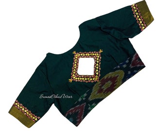 May include: A dark green blouse with a square neckline and short sleeves. The blouse features a decorative design on the back with gold and red beads. The blouse is made from a soft, silky fabric. "Sumas Ethnic Wear" is printed on the front of the blouse.