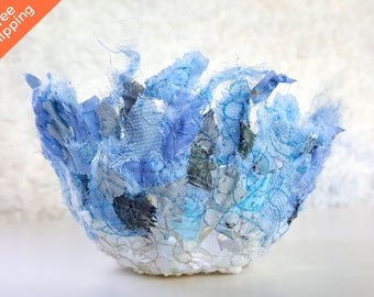 Puede incluir: Un pequeño cuenco azul y blanco hecho de retazos de tela. El cuenco tiene forma de flor y un borde delicado y rizado.