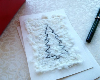 Puede incluir: Una tarjeta blanca con un contorno negro de un árbol de Navidad sobre un fondo blanco texturizado.