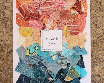 Puede incluir: Una tarjeta de felicitación blanca con un collage de retazos de tela variados en tonos naranja, rosa, amarillo y azul. Las piezas de tela están cosidas a la tarjeta con hilo dorado. Un pequeño cuadrado blanco con el texto thank you está centrado.