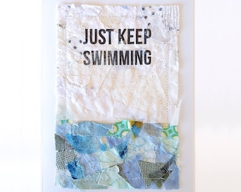 Puede incluir: Una tarjeta blanca con un collage de tela azul y verde. La tela está dispuesta para parecer agua. El texto "JUST KEEP SWIMMING" está impreso en negro en la parte superior de la tarjeta.