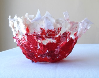 Puede incluir: Un cuenco de tela rojo y blanco hecho de trozos de tela cosidos juntos. El cuenco tiene forma de flor y tiene un aspecto delicado y aireado.