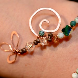 May include: A copper wire bracelet with green and white stones, a spiral charm, and a dragonfly charm.