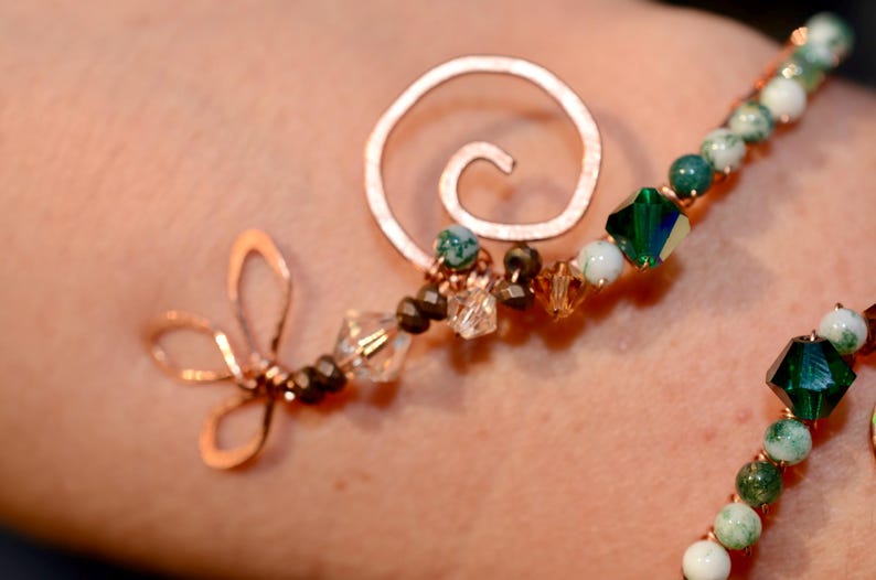 May include: A copper wire bracelet with green and white stones, a spiral charm, and a dragonfly charm.