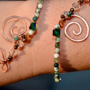 May include: A copper wire bracelet with green and white agate beads, copper swirls, and a copper butterfly charm.