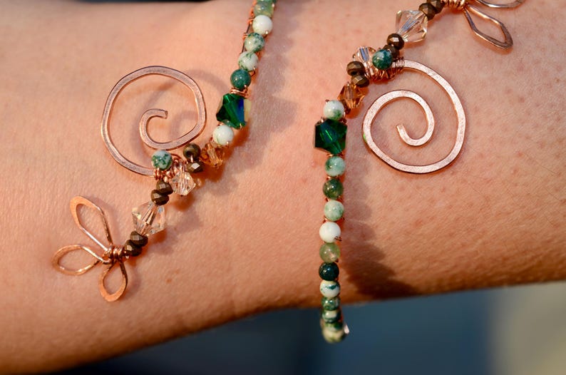 May include: A copper wire bracelet with green and white agate beads, copper swirls, and a copper butterfly charm.