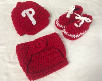 May include: Red crocheted baby outfit with a hat, diaper cover, and booties. The hat features a white "P" on the front.