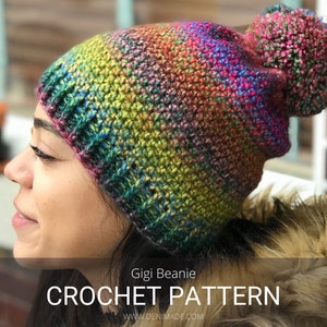 Può includere: Un berretto all'uncinetto colorato con un pompon soffice. Il berretto è realizzato con un filato arcobaleno e ha una combinazione di colori verde, blu e viola. Il berretto è indossato da una persona con i capelli castani. Il testo sull'immagine dice "Gigi Beanie CROCHET PATTERN www.denimade.com".
