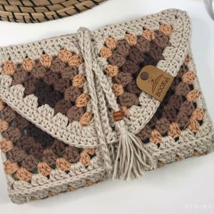 May include: A crocheted beige and brown book clutch with a tassel and a leather tag that says "BOOKISH".