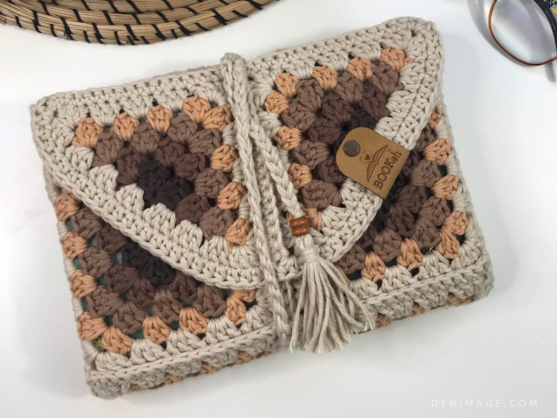 May include: A crocheted beige and brown book clutch with a tassel and a leather tag that says "BOOKISH".