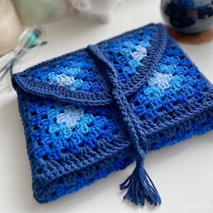 May include: A blue crocheted clutch bag with a tassel. The bag is made of granny squares in shades of blue.