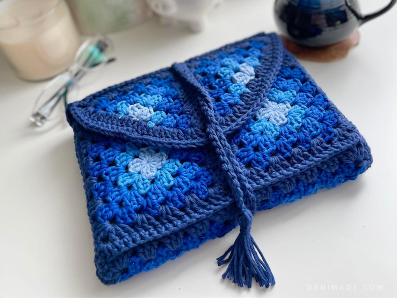 May include: A blue crocheted clutch bag with a tassel. The bag is made of granny squares in shades of blue.