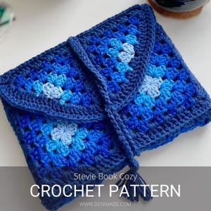 May include: A blue crocheted book cosy with a granny square pattern and a tassel. The cosy is folded and has the text "Stevie Book Cozy CROCHET PATTERN www.DENIMADE.COM" on the bottom.