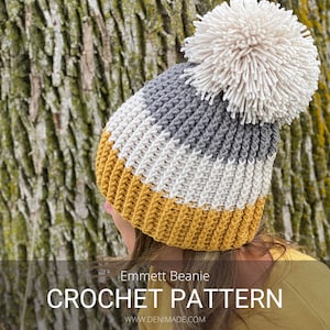 May include: A crochet beanie pattern for a striped beanie with a white pom pom. The beanie is in shades of gray, white, and yellow. The pattern is called "Emmett Beanie" and is available on the website www.denimade.com.