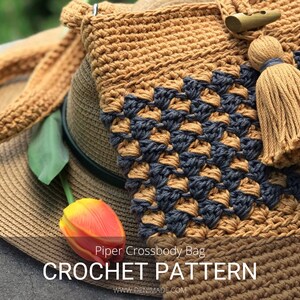 May include: A crocheted crossbody bag with a brown and blue geometric pattern. The bag has a brown tassel and a brown leather strap. The bag is sitting on a straw hat with a flower.