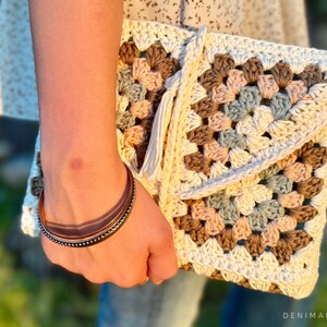 May include: A crocheted clutch bag with a granny square pattern in shades of brown, beige, and blue. The bag has a white tassel.