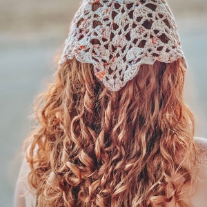 May include: A woman with long, curly, auburn hair is wearing a white crocheted headband with a floral pattern.