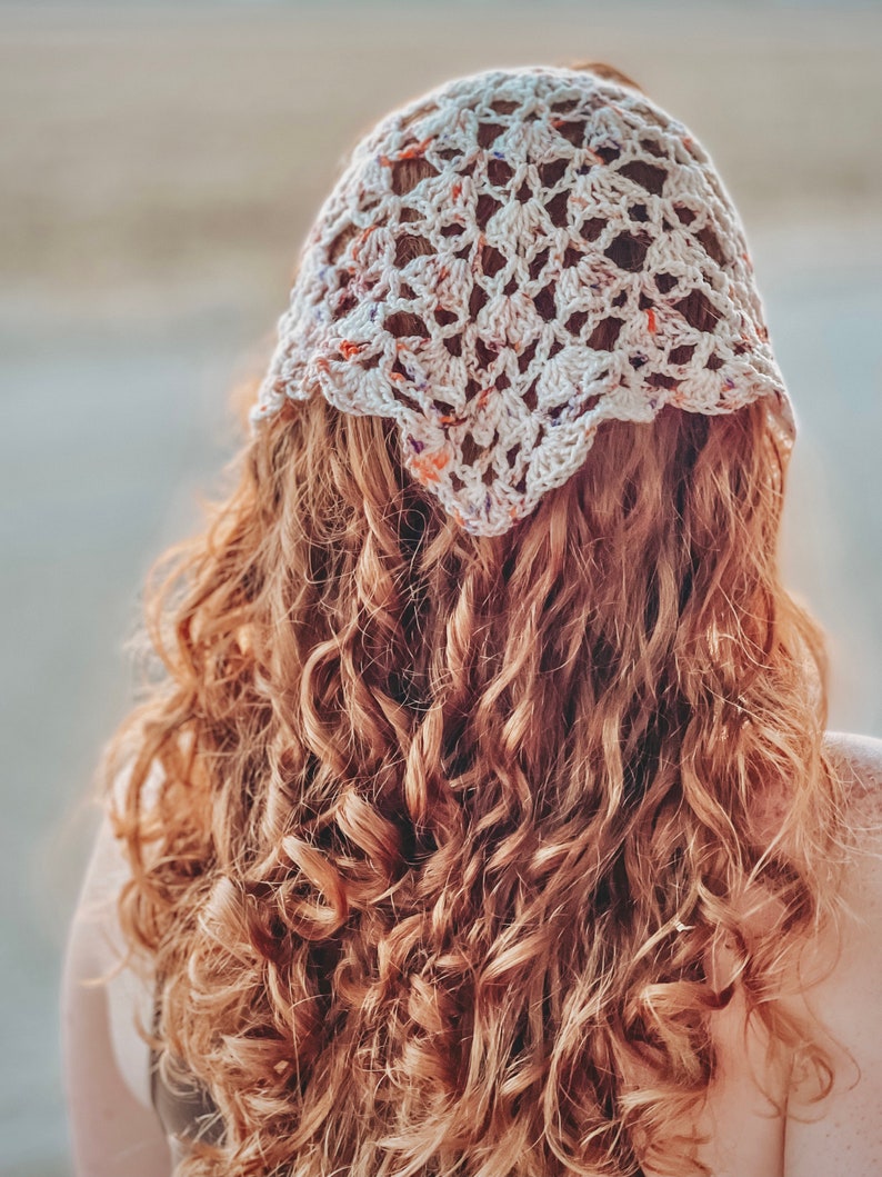 May include: A woman with long, curly, auburn hair is wearing a white crocheted headband with a floral pattern.