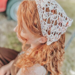 May include: A white crocheted headband with a lacy pattern and colorful flecks. The headband is worn by a person with long, curly red hair.