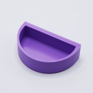 May include: A purple half-circle shaped dish with a smooth, slightly textured surface. The dish is made of plastic and has a rounded edge.