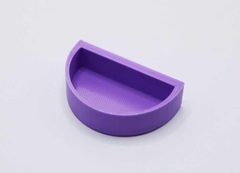 May include: A purple half-circle shaped dish with a smooth, slightly textured surface. The dish is made of plastic and has a rounded edge.
