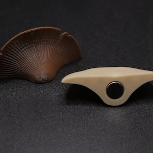 Op de afbeelding: Twee decoratieve objecten, een bruin en een beige, met een magneet op het beige object.