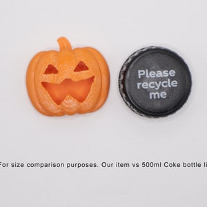 May include: An orange plastic jack-o'-lantern with a carved face, next to a black plastic bottle cap with the text "Please recycle me".