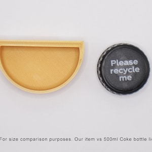 May include: A half-circle wooden tray next to a black plastic bottle cap with the text "Please recycle me". The tray is about the same size as a 500 ml Coke bottle lid.
