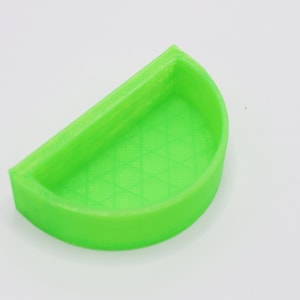 May include: A bright green plastic half-circle dish with a textured surface. The dish is designed to hold small items.