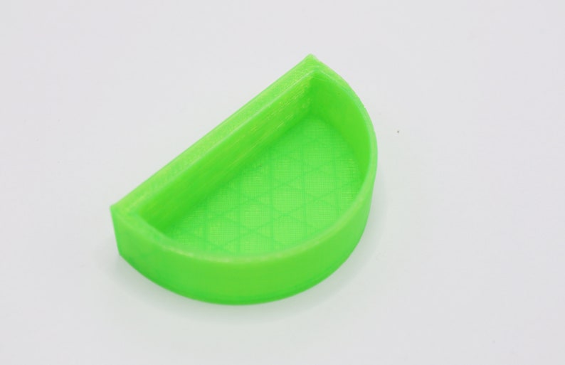 May include: A bright green plastic half-circle dish with a textured surface. The dish is designed to hold small items.