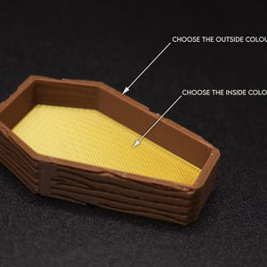 Op de afbeelding: Een klein houten doosje in de vorm van een kist met een getextureerd houtnerfdesign. De binnenkant van het doosje is effen geel. Kies de buiten- en binnenkleuren.