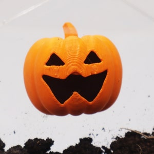 May include: An orange plastic jack-o'-lantern with a carved face. The pumpkin is floating above a pile of brown dirt.