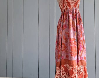 May include: A floor-length sleeveless maxi dress featuring a vibrant orange, pink, and white floral and paisley pattern. The garment has a square neckline, thin shoulder straps, and a gathered bodice that flows into a loose, tiered skirt.