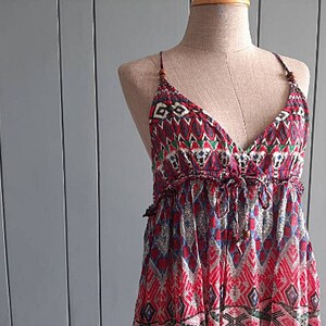 May include: A red, blue, and green patterned maxi dress with a V-neckline and thin straps. The dress has a bohemian style and is made of a lightweight fabric.