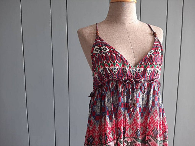 May include: A red, blue, and green patterned maxi dress with a V-neckline and thin straps. The dress has a bohemian style and is made of a lightweight fabric.