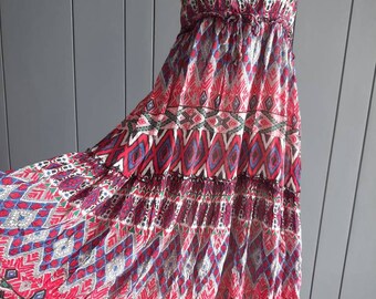 Könnte beinhalten: Ein langes, fließendes Maxikleid mit einem farbenfrohen geometrischen Muster. Das Kleid hat einen V-Ausschnitt und dünne Träger. Das Muster ist eine Mischung aus Rot, Blau, Grün und Schwarz.
