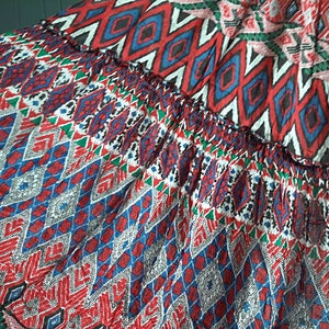 May include: Close-up of a colorful fabric with a geometric pattern in shades of red, blue, green, and white. The fabric has a ruffled edge.