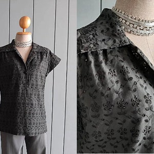 Puede incluir: Una blusa negra de manga corta con cuello y estampado floral. La blusa tiene cierre de botones en la parte delantera y una silueta ajustada.
