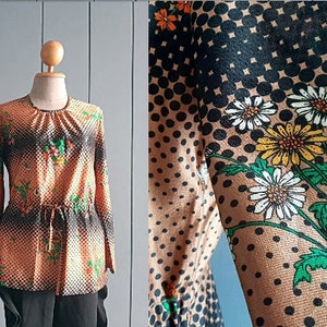 May include: A brown and black patterned blouse with a drawstring waist. The pattern features small black dots, white daisies, and yellow flowers.