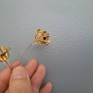 May include: A pair of gold-toned stud earrings shaped like open flower blossoms. Each earring features delicate, thin metal petals radiating outward from a central point, finished with small, rounded tips and clear plastic earring backs.