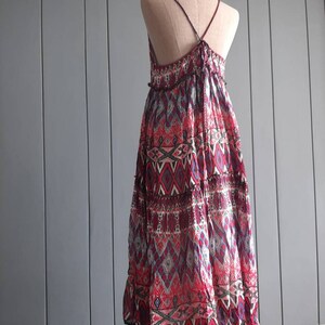May include: A long, flowy dress with a geometric print in shades of red, blue, and white. The dress has a halter neckline and a tiered skirt.