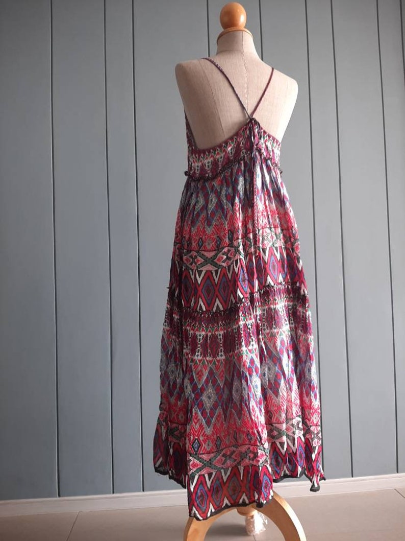 May include: A long, flowy dress with a geometric print in shades of red, blue, and white. The dress has a halter neckline and a tiered skirt.