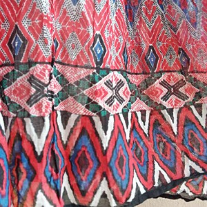 May include: Close-up of a red, white, blue, and black patterned fabric with a geometric design. The fabric is sheer and has a slightly wrinkled texture.