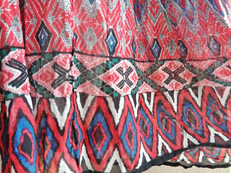 May include: Close-up of a red, white, blue, and black patterned fabric with a geometric design. The fabric is sheer and has a slightly wrinkled texture.